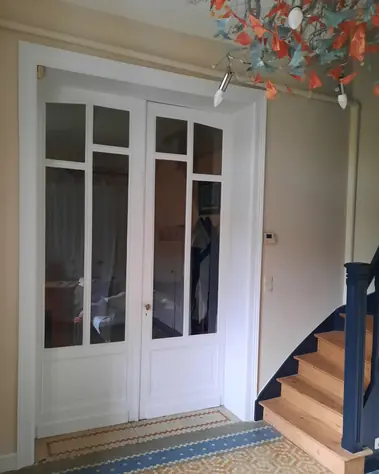 Peinture blanche sur portes vitrées et chambranle, escalier avec limon bleu et sol en mosaïque.