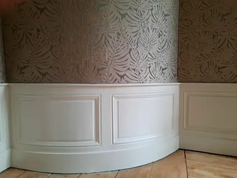 Papier peint motif feuilles et moulures blanches sur parquet en angle.