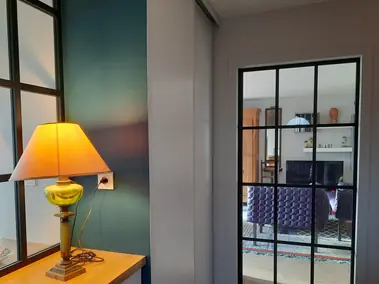 Peinture murale bleu canard et cloison gris clair, porte vitrée aluminium noir.